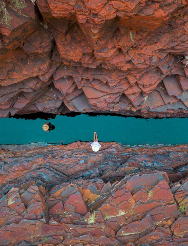 Overhead shot of two people in a narrow section of Weano Gorge, Karijini National Park. One is walking along the gorge floor, through water, and one is relaxing on the rocks.