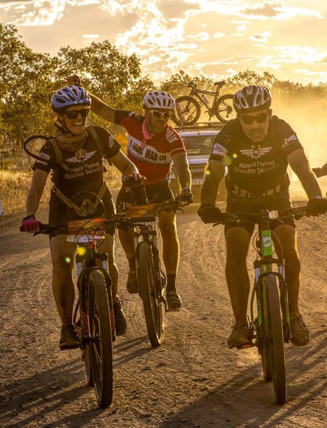 4 cyclists with their support vehicle behind riding on the Gibb River Road at sunset