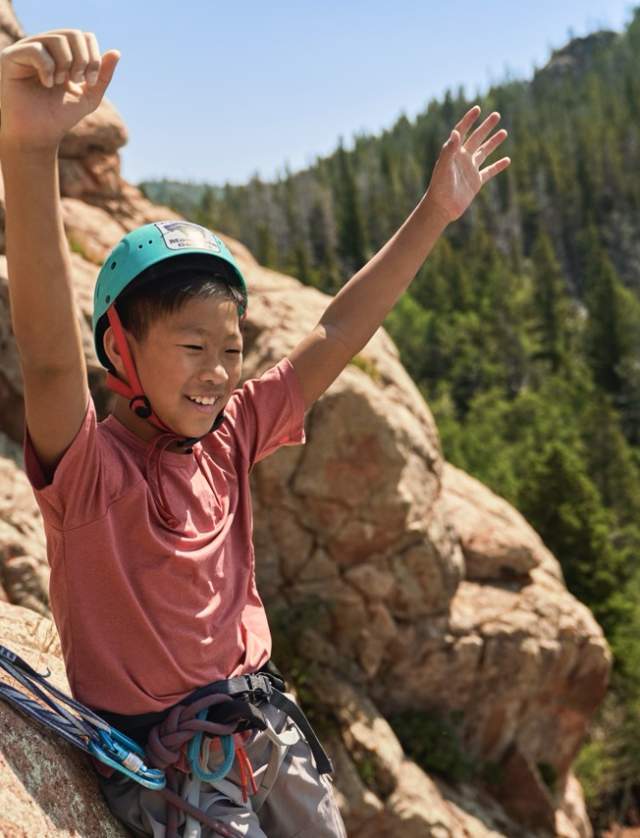child with arms above head smiling and celebrating with rock climbing gear on