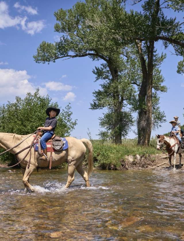 people on horseback wading into water