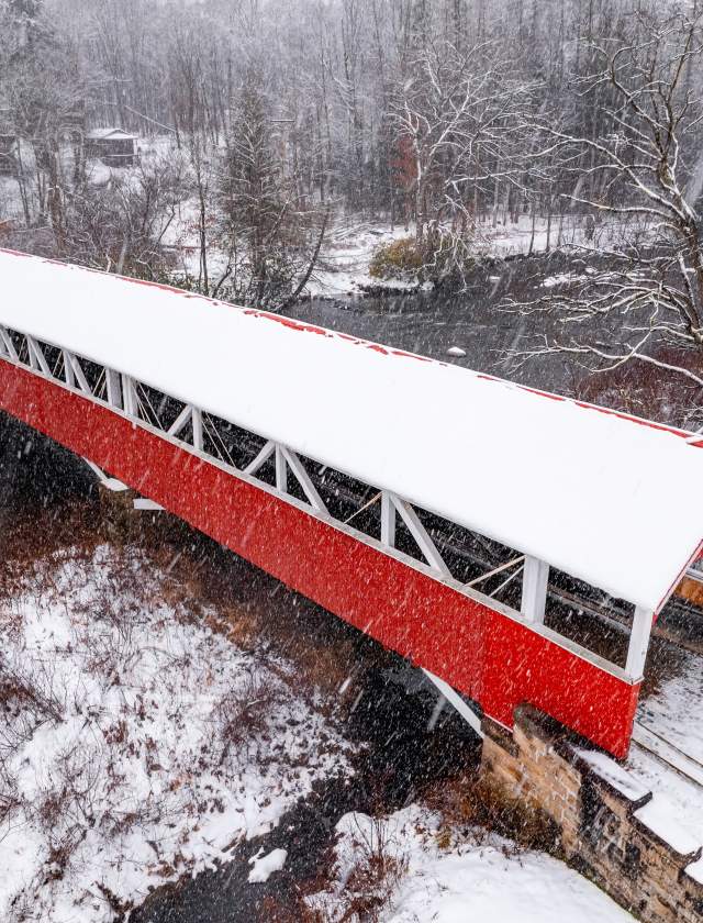 Birds eye view of a snow covered red covered bridge over a river in the Laurel Highlands