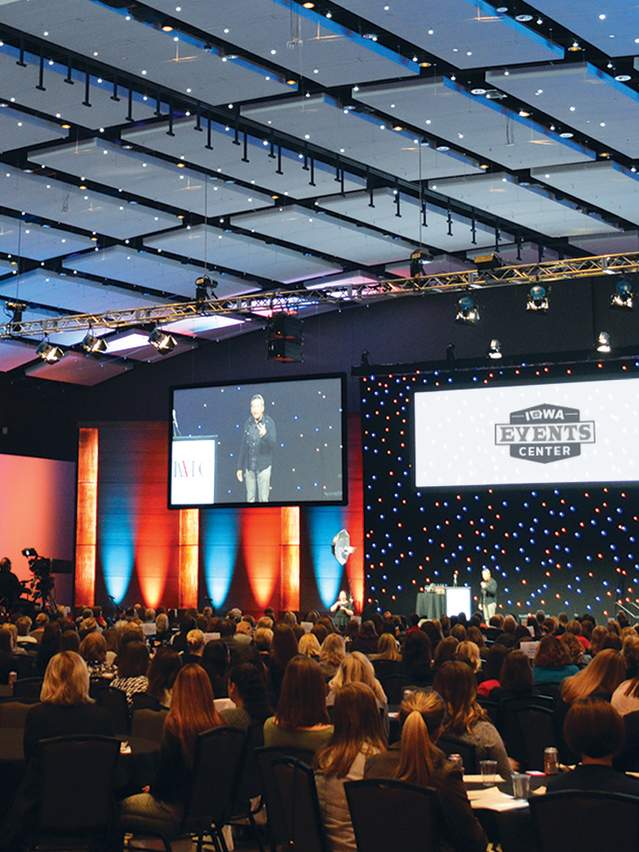 Man speaking on stage to a large room of attendees at the Iowa Events Center