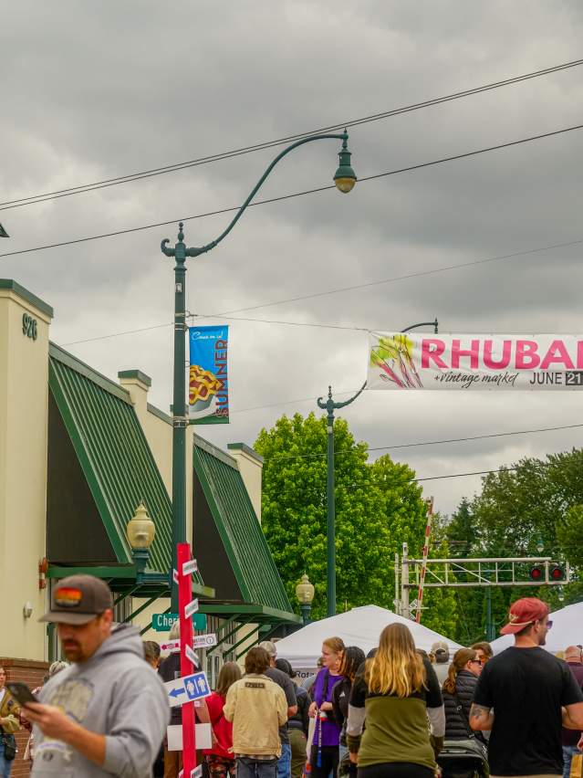 A crowd walking down Main Street during Rhubarb Days in Sumner, Washington, with the Rhubarb Days banner overhead.