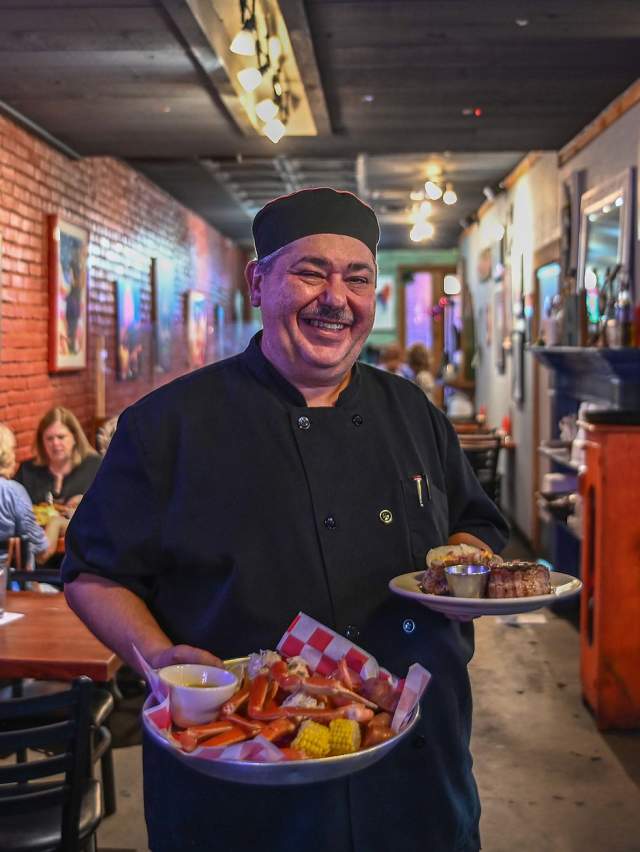 The chef at AJs Oyster House in Fort Smith, Arkansas is holding an enticing plate of crab legs and a plate of steak.