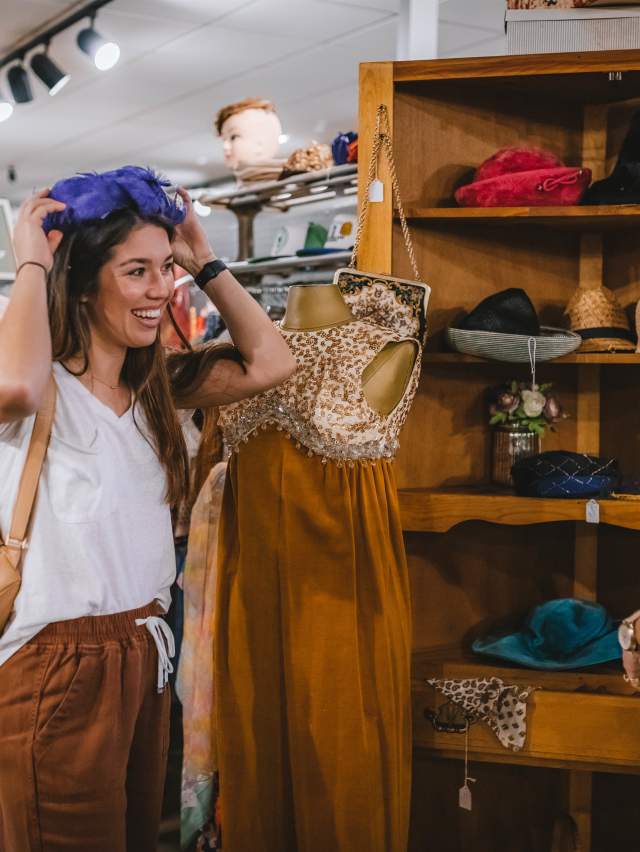 A mother looks at shelves full of vintage hats as a daughter smiles and tries one on at Belle Starr Antiques in Fort Smith.