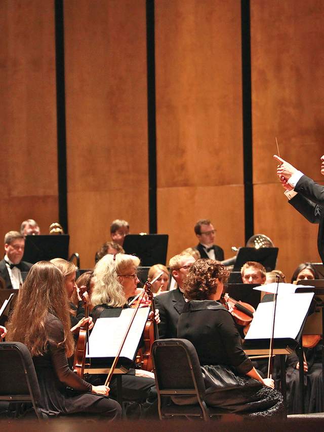 The conductor of the Fort Smith symphony has his baton raise, ready to conduct the symphony in front of him.