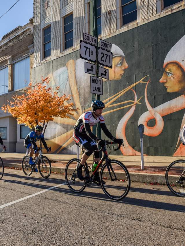 Road bikers bike past a colorful mural painted on a brick building in Fort Smith.