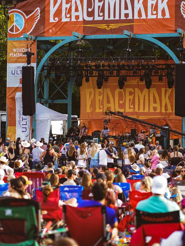 A crowd of people enjoy a band performing on a vibrant stage at Peacemaker Music Festival in Fort Smith.