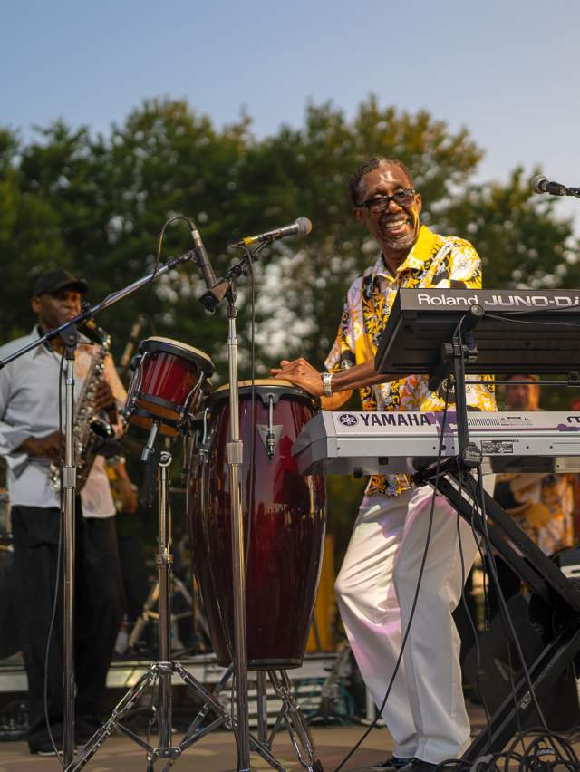 A man plays the saxophone while another man plays the drums on stage at Fort Smith's 4th of July event.