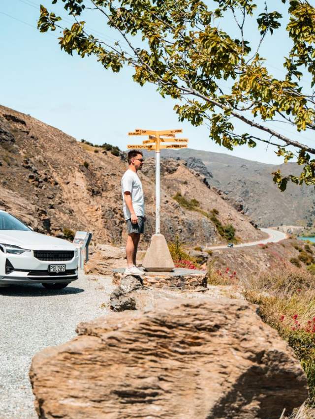 Man standing a highway lookout next to parked EV near Cromwell