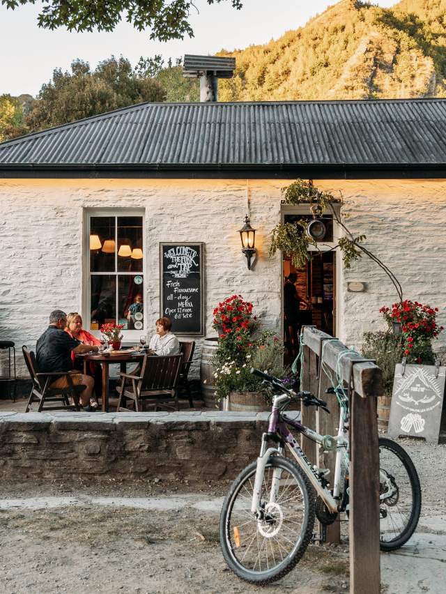 Old white cottage-looking pub with people sitting al fresco and green mountains in the background