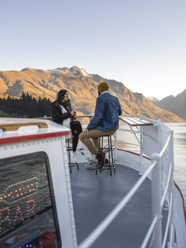 A couple sitting on the front of Perky's Floating Bar in Winter with lake and mountain views