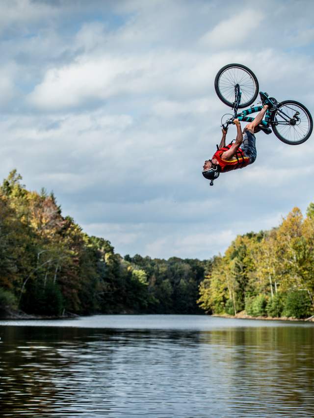 Stunt biker going off a ramp and flipping upside down over water at Griffin Bike Park, Terre Haute, Indiana