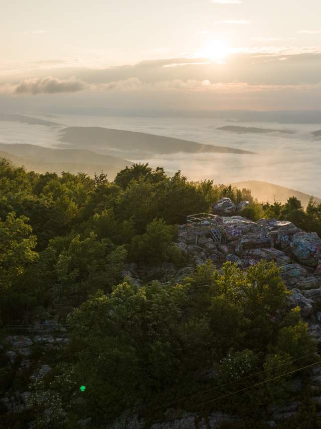 Sunrise over the Appalachian Mountains from Dan’s Rock Scenic Overlook in Dans Mountain State Park, with a rocky viewing platform surrounded by forest and a valley filled with morning fog.