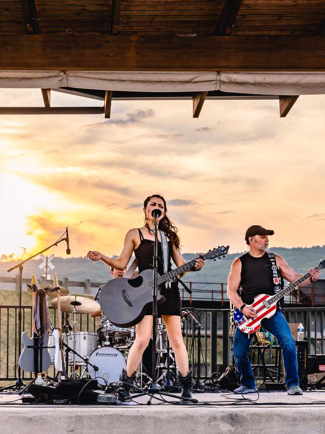 Female lead singer and her band perform at sunset on an open-air stage.
