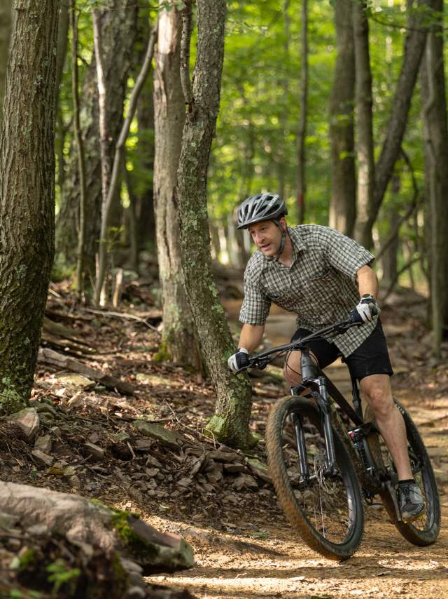 A man rides a bike on a rough mountain trail through the woods.