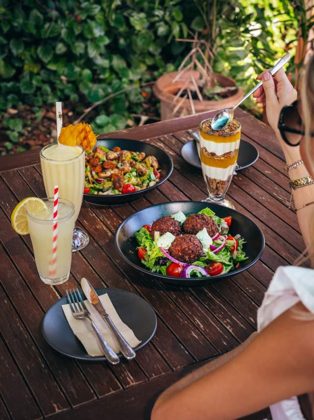 A woman sits at a table in the Ivanhoe Cafe, with a spread of lunch dishes and drinks in front of her