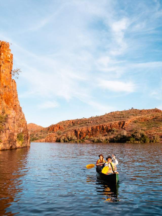 Econoeing tour on the Ord River in Kununurra - two paddlers on the river alongside a tall red cliff