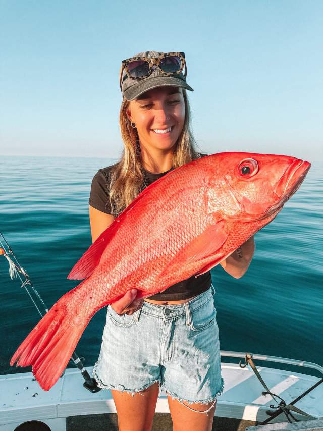 A woman in a boat holding a freshly caught Red Emporer