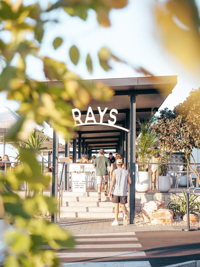 Two men walk up the steps to the restaurant at the Hedland Hotel, beneath a sign that says 'Rays'.