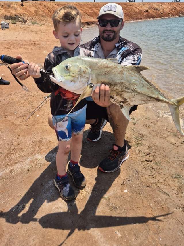 A child holding a Trevally, freshly caught from the shore at Port Hedland. A man crouches behind the child, supporting him