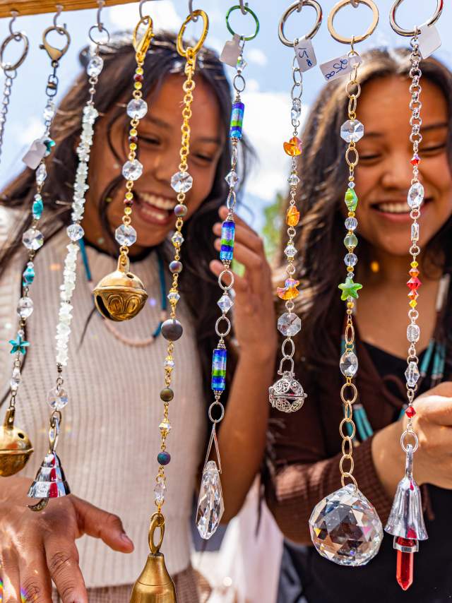 two smiling girls stand in front of a display of necklaces and pendants