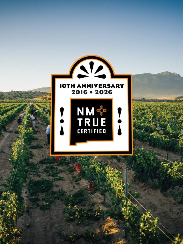 A vast vineyard stretches under a clear sky, with mountains in the background. In the center, there's a large "NM True Certified" logo celebrating its 10th anniversary from 2016 to 2026.