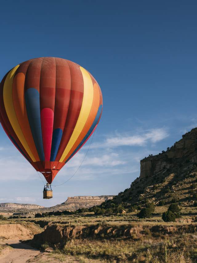 A colorful hot air balloon floats in a clear blue sky above a rugged landscape with rock formations.
