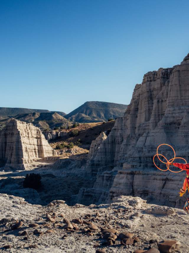 A traditional Native hoop dancer in a valley of rocks with mountains in the far distance