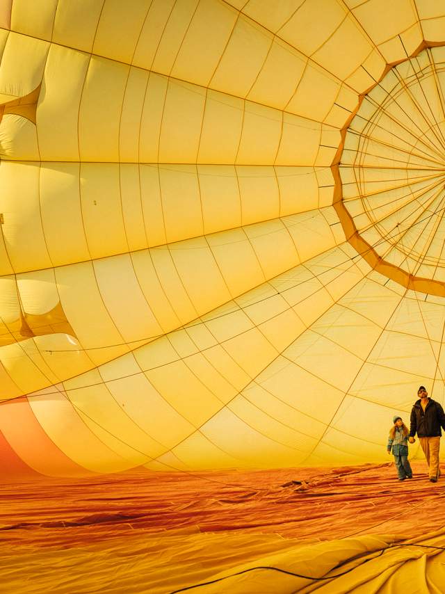 two people walk on the inside of a giant yellow and orange hot air balloon as it inflates on the ground