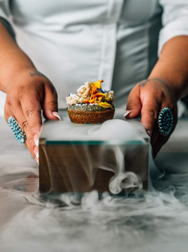 Chef preparing a dish with dry ice smoke effect in a professional kitchen.