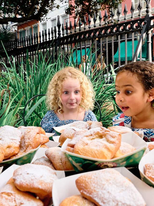 Two Children sit in front of a table of $100 of Beignets at Cafe Beignet in New Orleans' French Quarter.