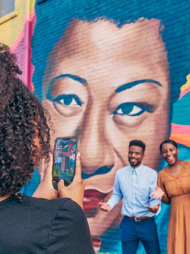 3 Friends Pose in front of Street Art mural while a person takes a photo