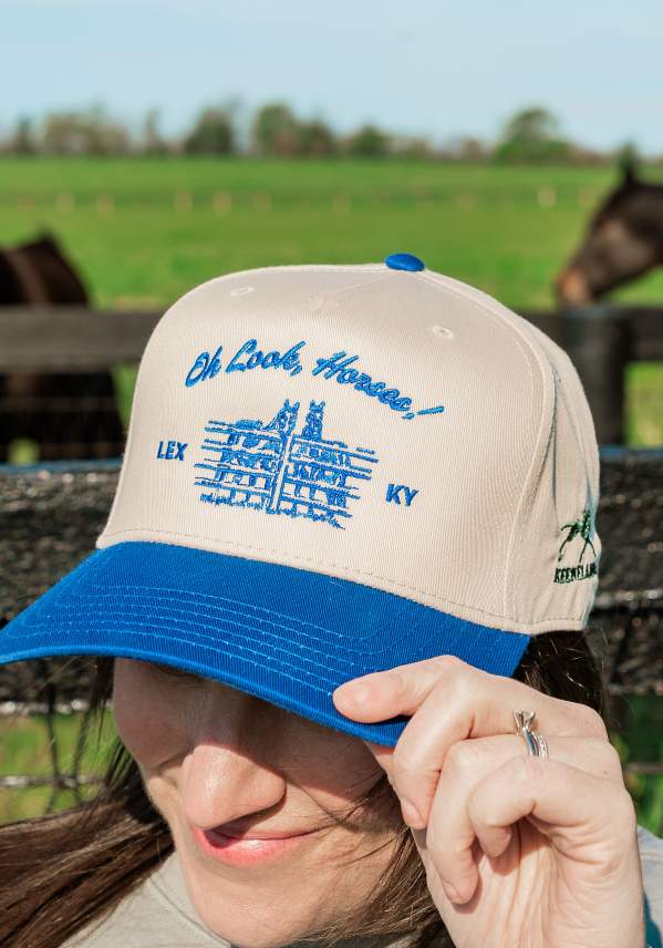 A woman wearing a blue and white trucker hat with a Lexington, KY horse illustration.