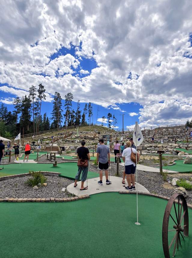 Family playing mini golf at Meandering Moose in Grand Lake under a bright blue sky