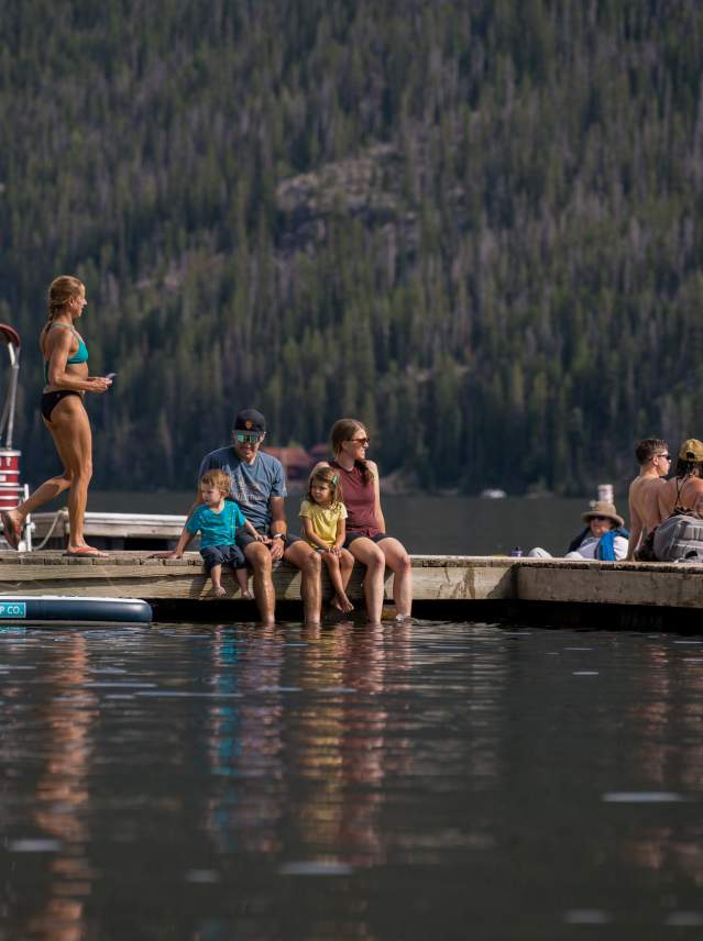 Families recreating on the L Dock in Grand Lake - paddleboarding, swimming, boating, dipping their feet in the lake.