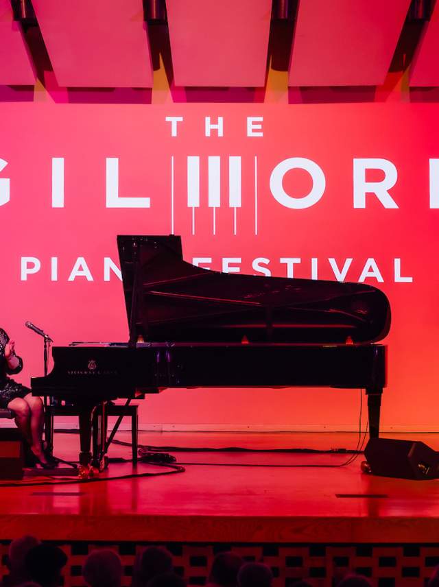 The Gilmore Piano Festival photos features a red-lit stage with a grand piano on stage.