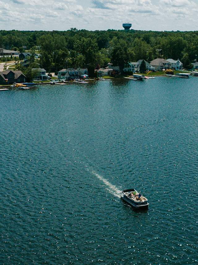 A white boat moves across  Gourdneck Lake, a vibrant blue lake in Portage, MI.