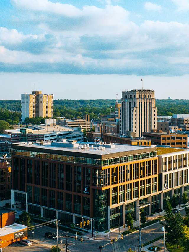 An aerial shot of Downtown Kalamazoo showcases a blue sky over the buildings, river, and Arcadia Creek Festival Place in Downtown Kalamazoo.