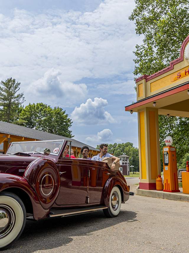 A man and a woman sit in a vintage car outside of a vintage Shell gas station located at the Gilmore Car Museum.