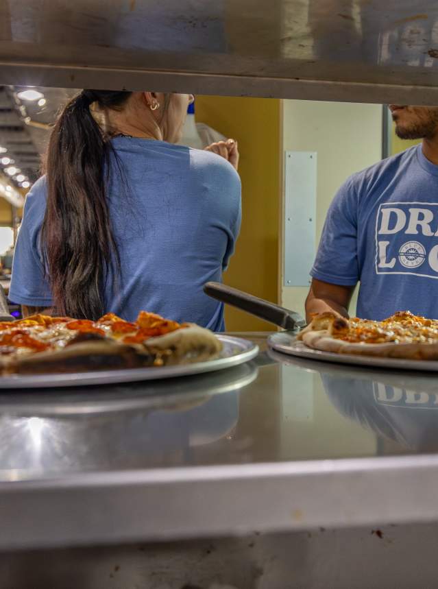 Pizza in a service window with staff in the background