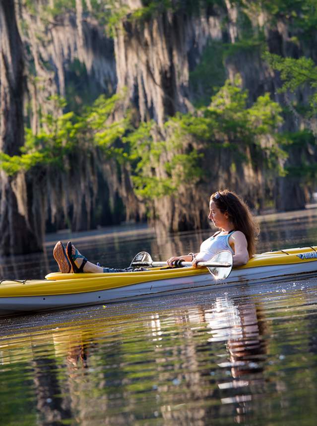Kayaker on lake under cypress trees with hanging Spanish moss