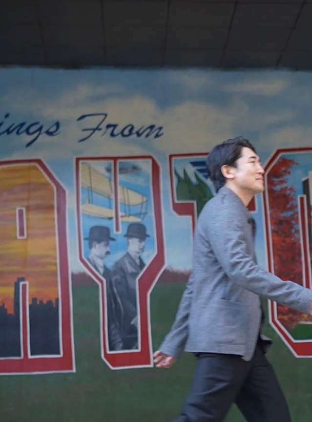 a man walking in front of a mural that says "greetings from dayton"