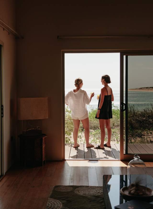 Two women stand in the doorway of a villa at Eco Beach Resort, overlooking the beach and Indian Ocean.