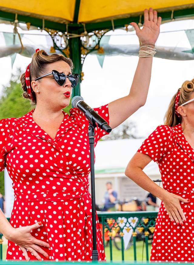 Two ladies wearing red polka dot dresses sing on a bandstand in Sussex