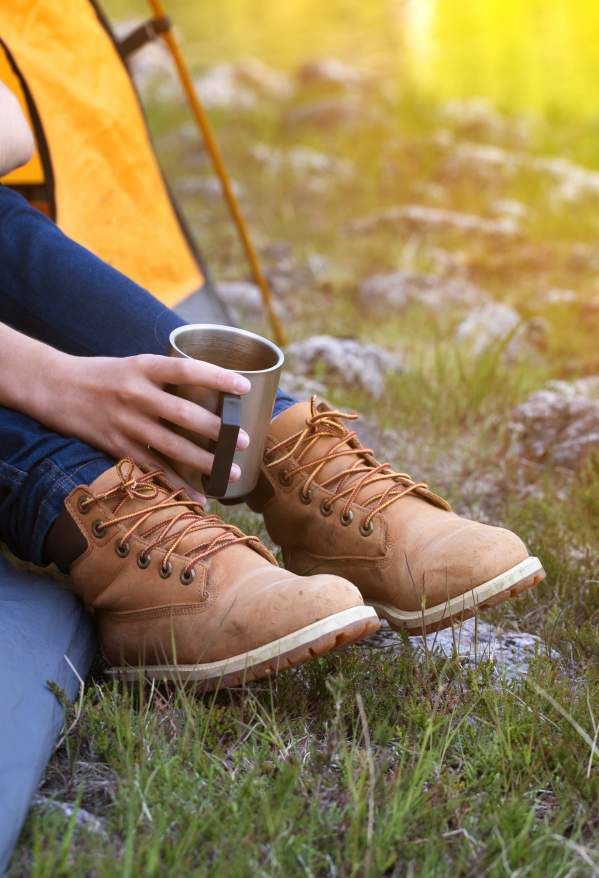 Someone sitting with their legs stuck outside of a tent while holding a coffee cup.