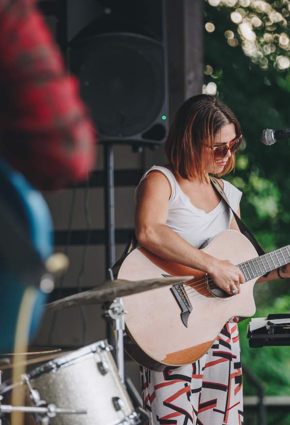 Woman wearing sunglasses playing a guitar with other band members nearby.