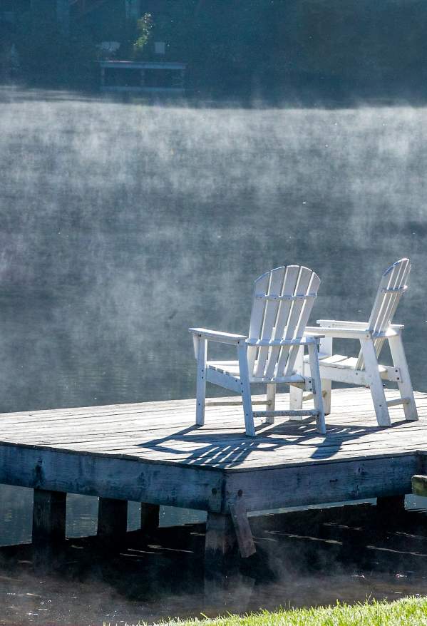 Two white adirondack chairs on a boat dock with a red canoe nearby.