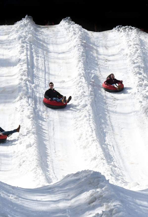 Four people snow tubing down a snowy hill.
