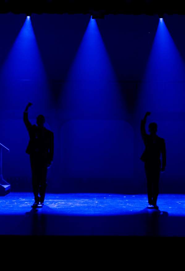 Sillouettes of four performers onstage underneath blue spotlights.